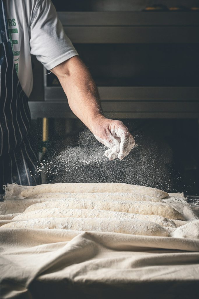Baker in an apron sprinkling flour over a worktable