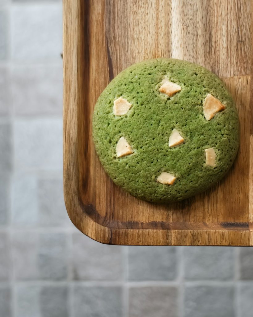 Green matcha cookie with white chocolate chips on a wooden board