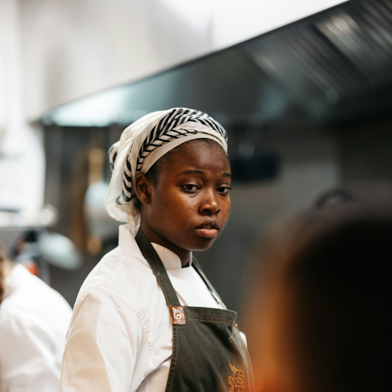Young chef in an apron and head wrap working in a kitchen