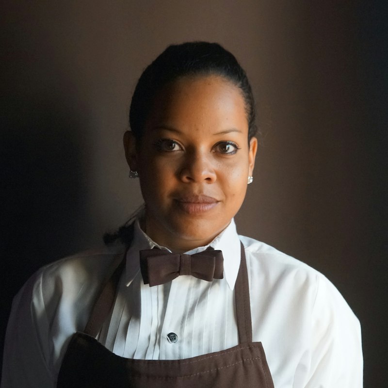 Front of house manager in a white shirt, bow tie and brown apron