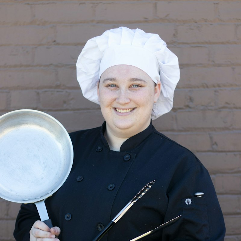 Smiling pastry chef in a white chef hat holding a pan